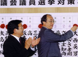 当選確実となった方にバラを付ける中川雅治
